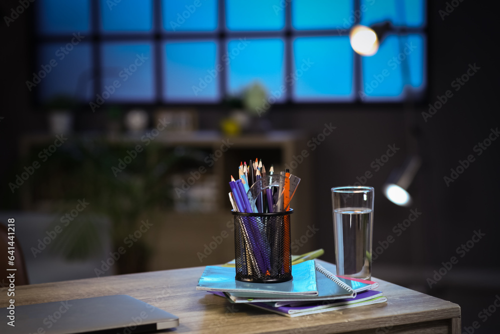 Workplace with lamp, glass of water and different stationery on table at night