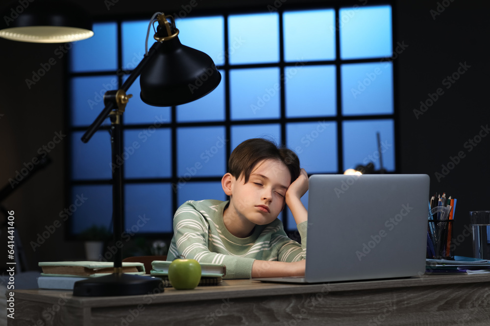 Sleepy little boy with doing homework at home late in evening