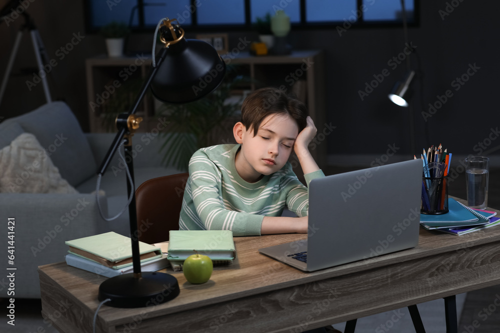 Sleepy little boy with doing homework at home late in evening