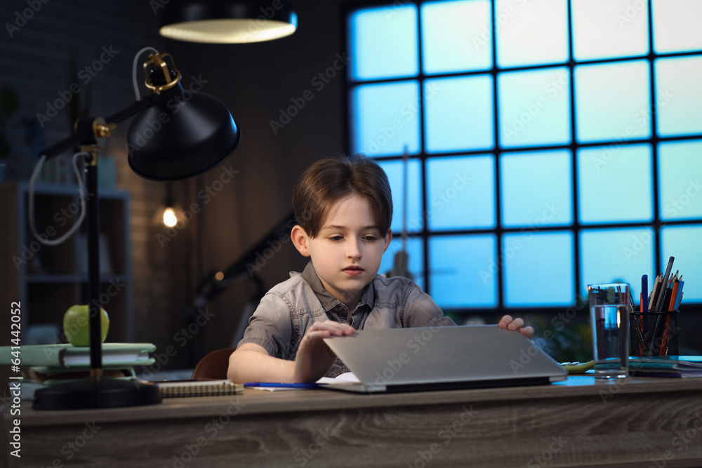 Little boy doing homework with laptop at home late in evening