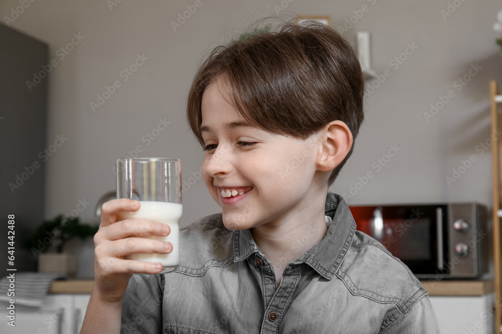 Happy little boy with glass of fresh milk in kitchen