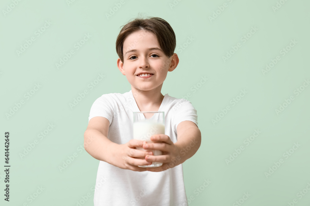 Happy little boy with glass of fresh milk on turquoise background