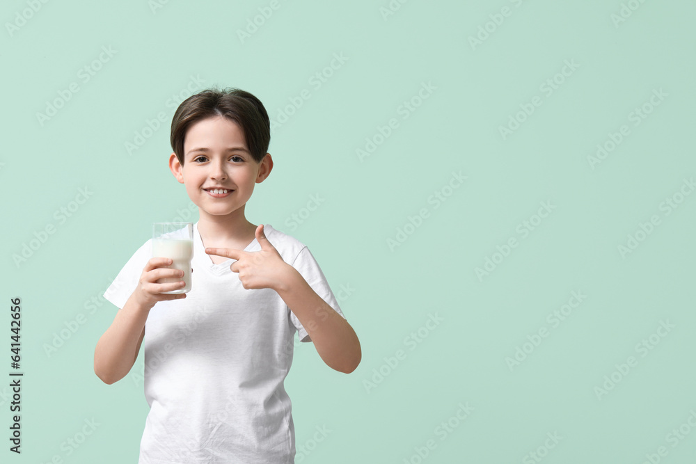 Happy little boy pointing at glass of fresh milk on turquoise background