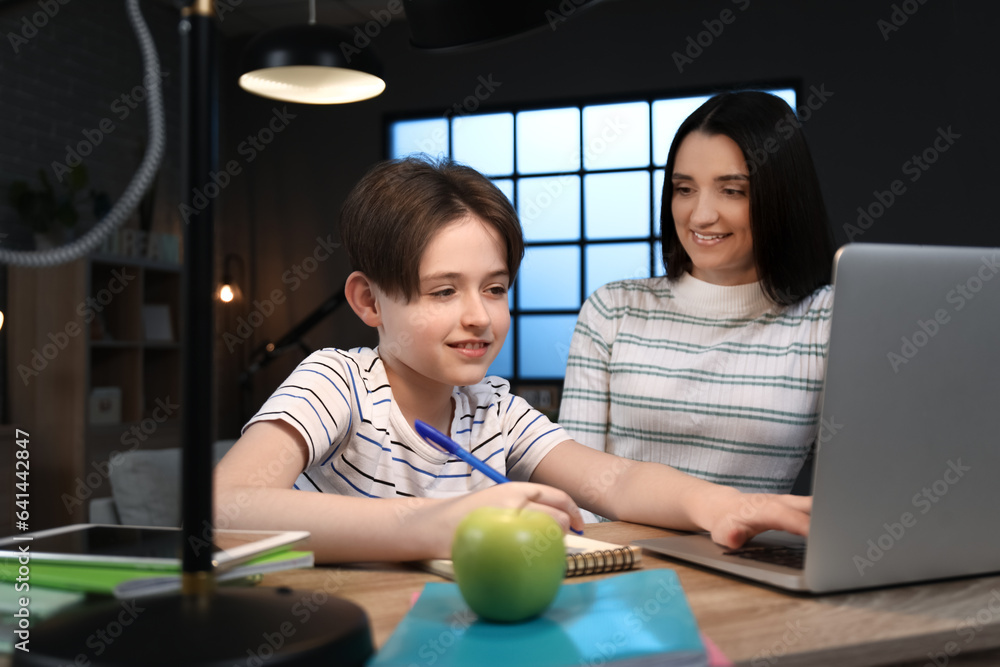 Mother with her little son sitting at table and doing homework late in evening