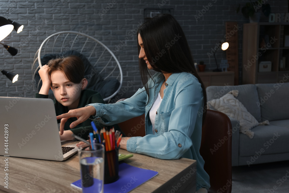 Mother with her little son sitting at table and doing homework late in evening