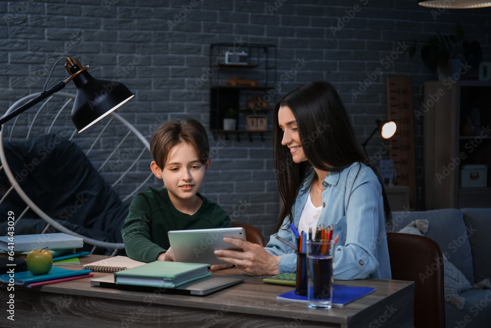 Mother and her little son doing homework with tablet late in evening