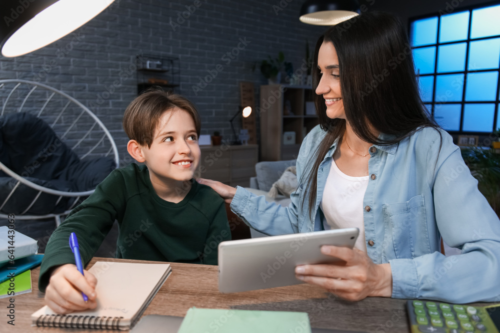 Mother and her little son doing homework with tablet late in evening