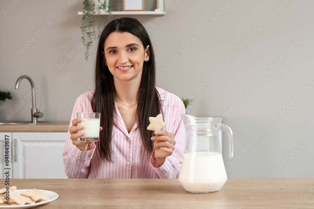 Beautiful woman with cookie and glass of fresh milk in kitchen