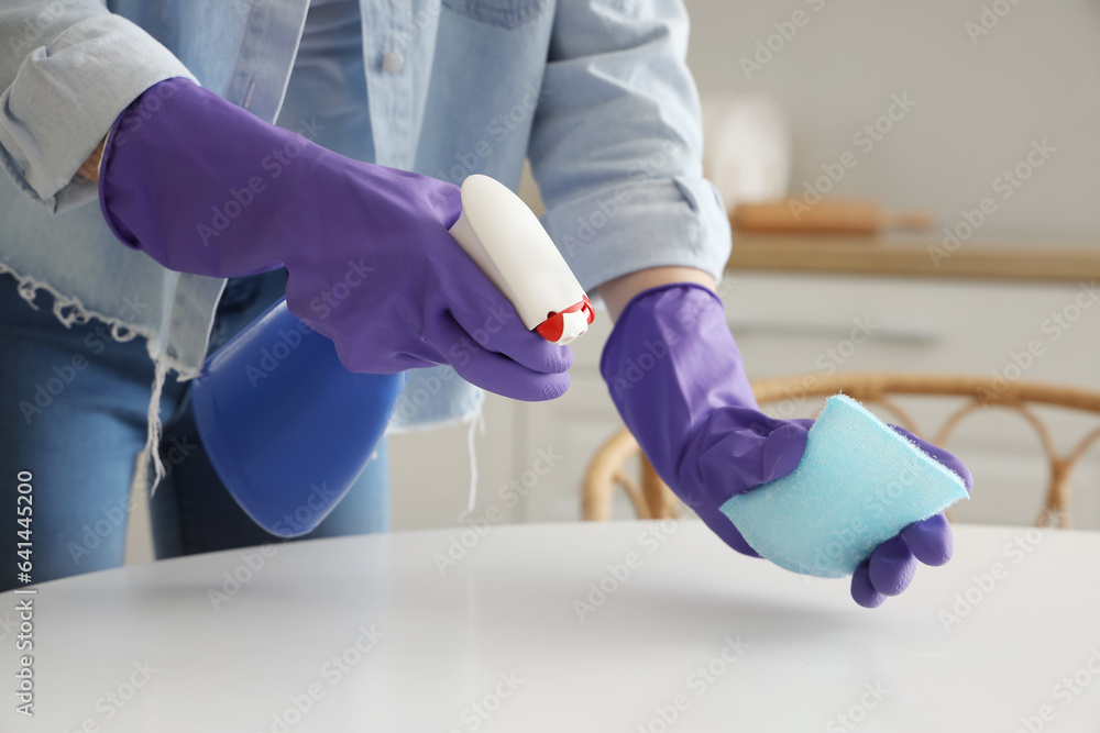 Woman in purple rubber gloves cleaning table with sponge and detergent