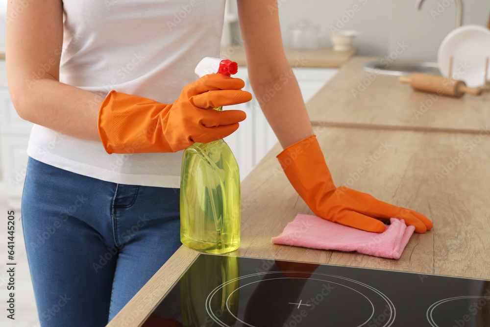 Woman in orange rubber gloves cleaning wooden countertop with rag and detergent