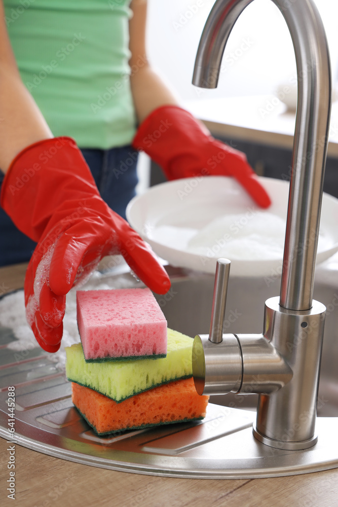 Woman in red rubber gloves washing dishes with sponge