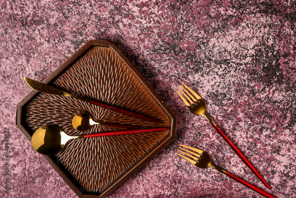 Clean plate with set of cutlery on dark pink table