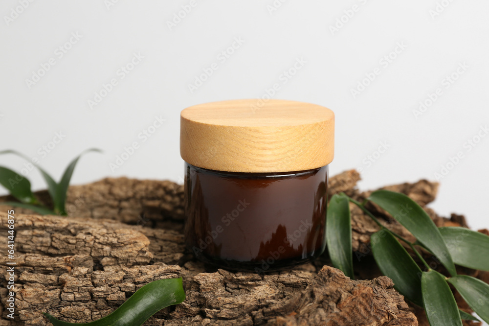 Jar of cosmetic product, tree bark and plant leaves on light background, closeup