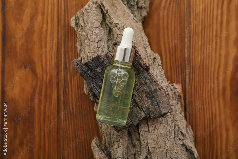 Bottle of essential oil and tree bark on wooden background, closeup