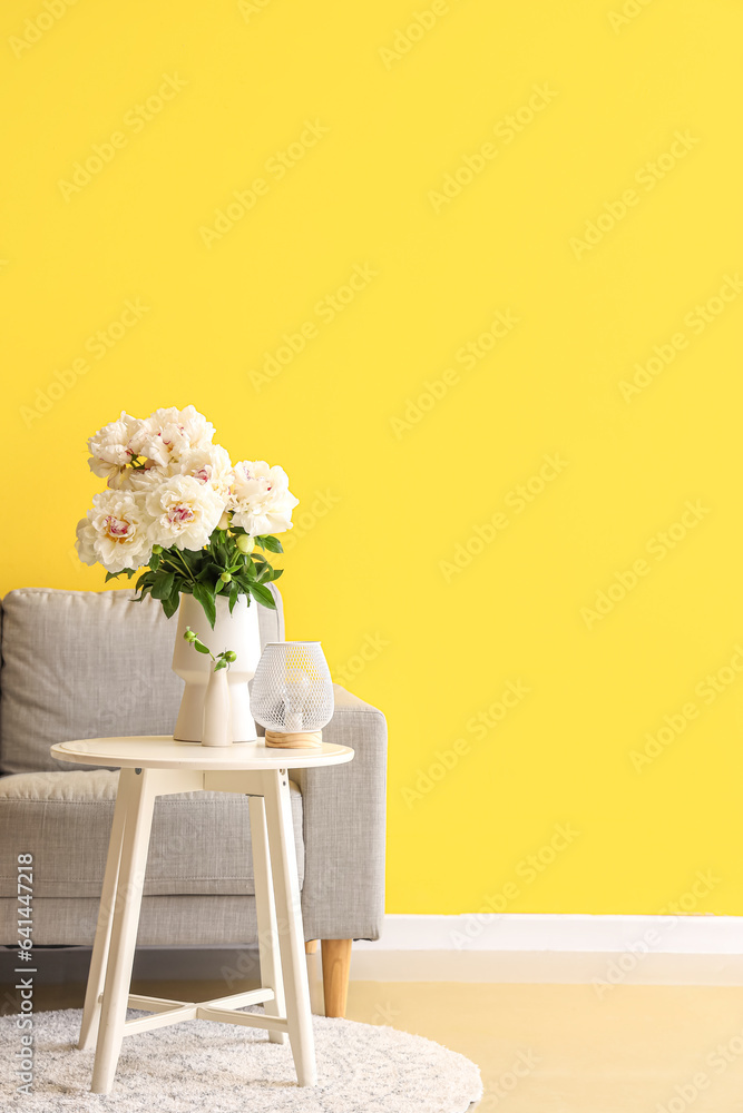 Vase of white peonies with coffee table and couch near yellow wall