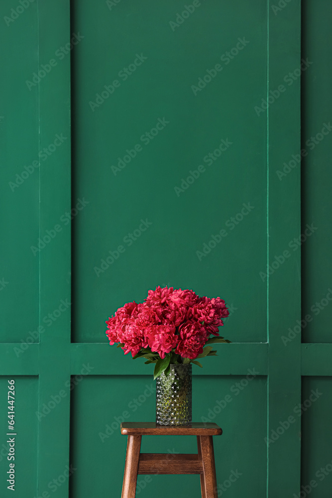 Vase of red peonies on stool near green wall