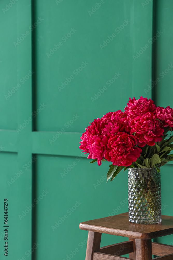 Vase of red peonies on stool near green wall