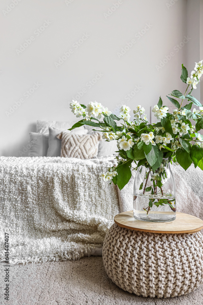 Vase with blooming jasmine flowers on pouf in interior of light bedroom