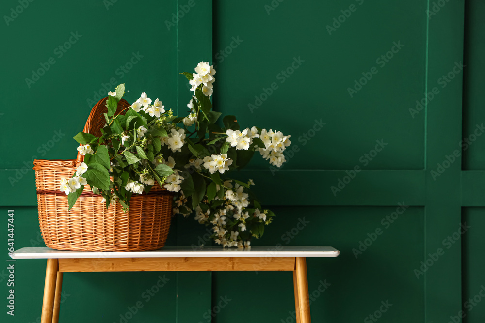 Wicker basket with blooming jasmine flowers on console table near green wall