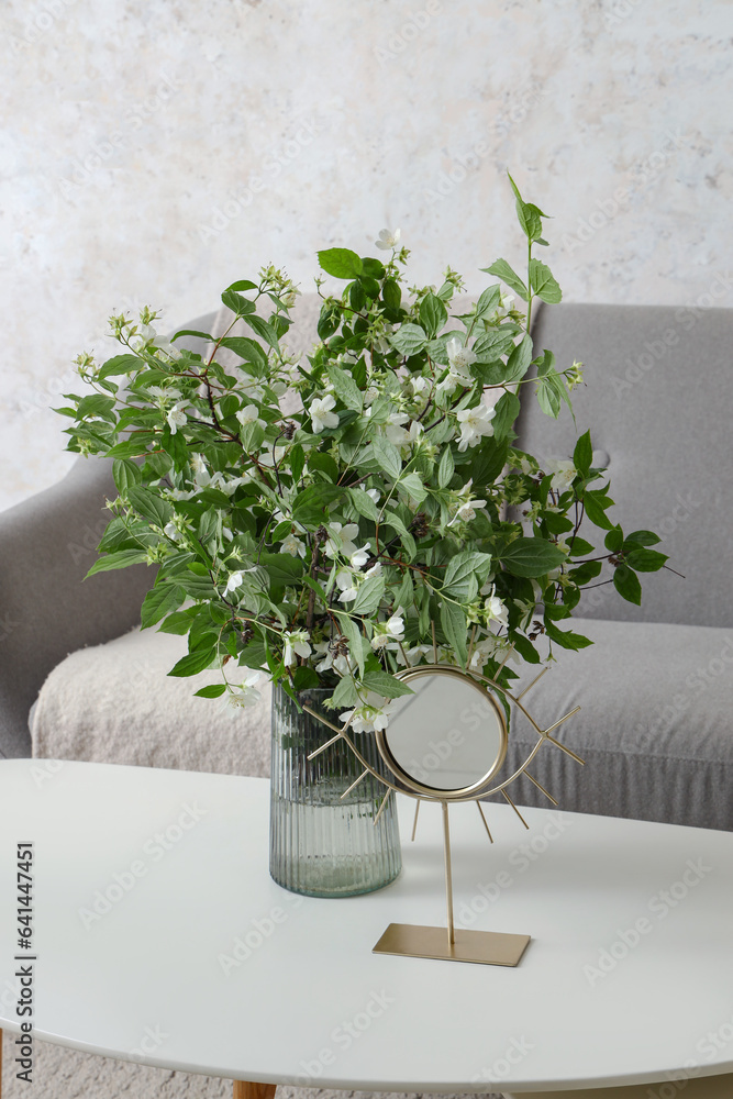 Vase with blooming jasmine flowers on coffee table in living room