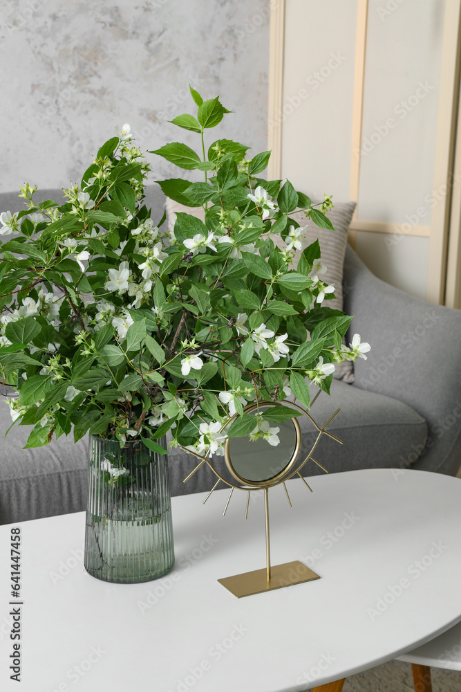 Vase with blooming jasmine flowers on coffee table in living room