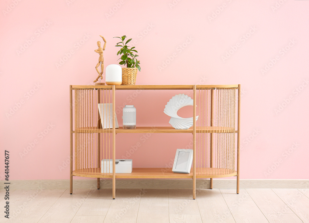 Modern shelving unit with houseplant and decor near pink wall in room