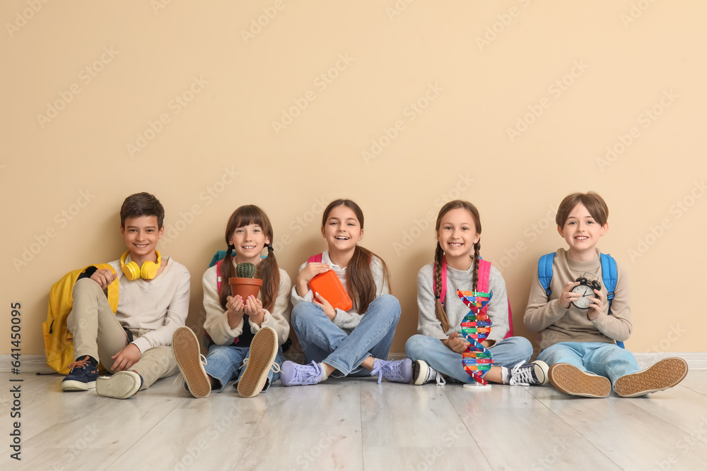 Little pupils with backpacks sitting near beige wall