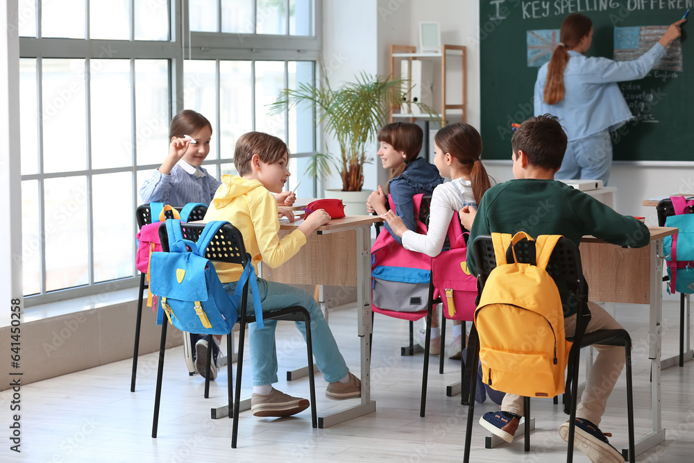 Little pupils with backpacks having lesson in classroom