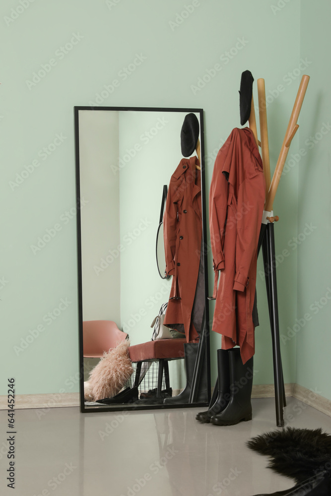 Mirror and rack with clothes near green wall in hallway