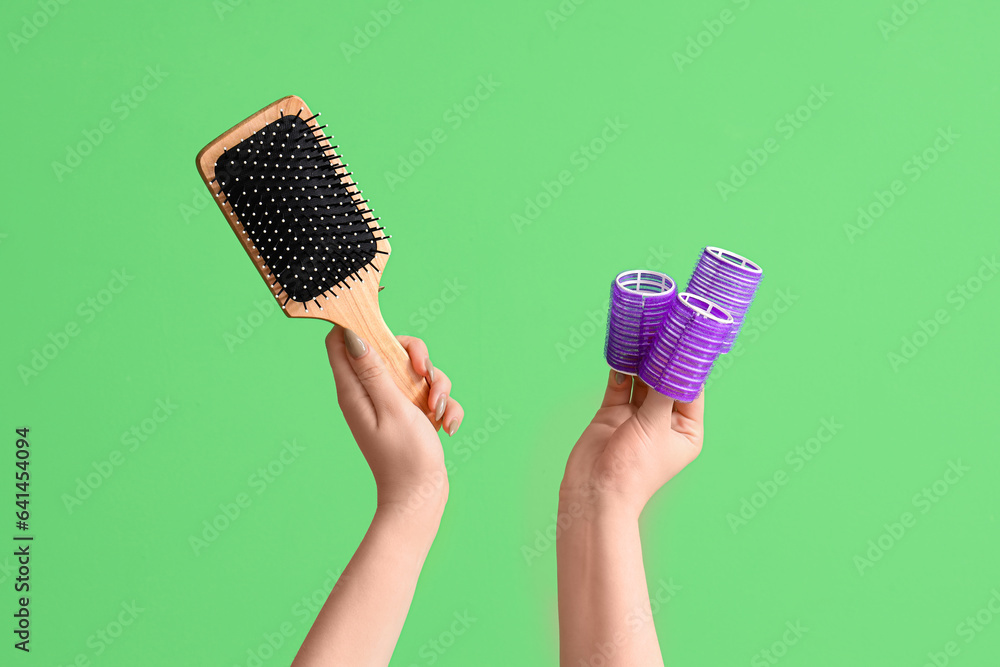 Female hands with paddle brush and curlers on green background