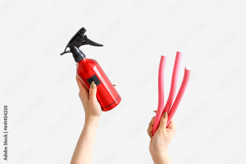 Female hands with hair spray and curlers on white background