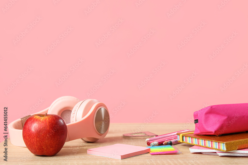 Modern school desk with headphones and stationery on pink background