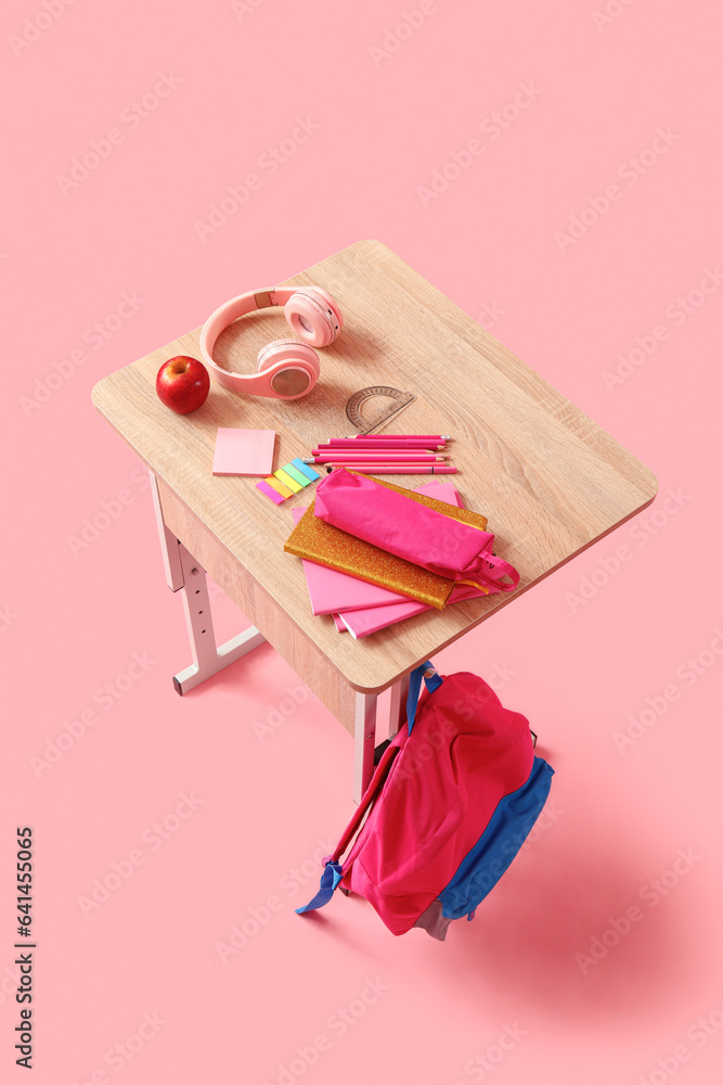 Modern school desk with backpack, headphones and stationery on pink background