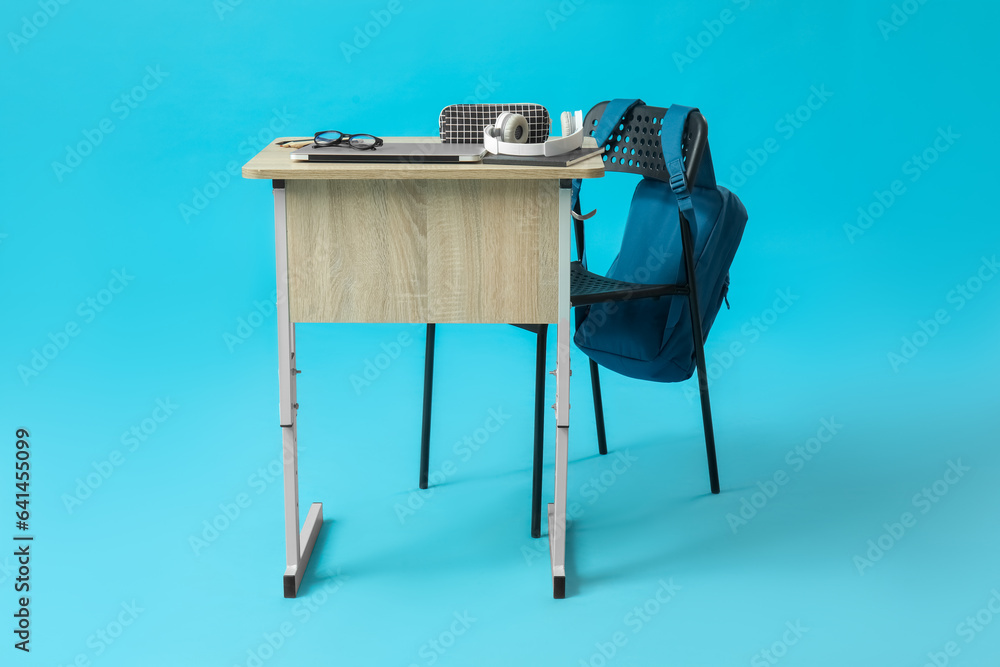 Modern school desk with backpack, laptop and stationery on blue background