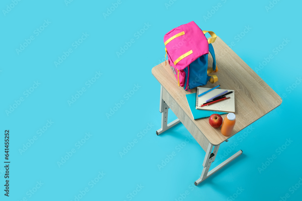 Modern school desk with backpack, lunch and stationery on blue background