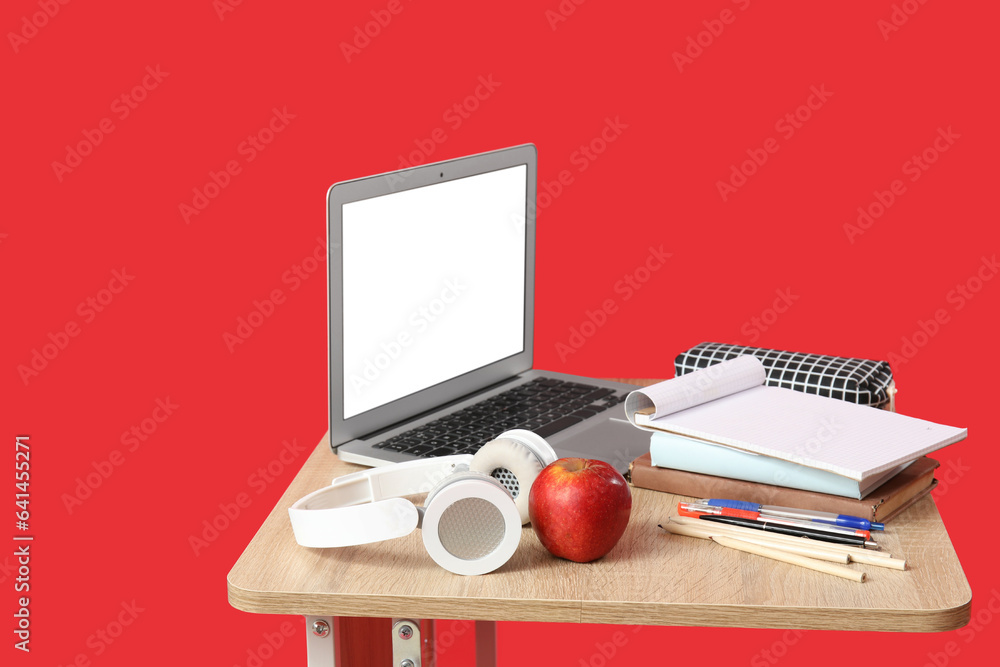 Modern school desk with laptop, headphones and stationery on red background