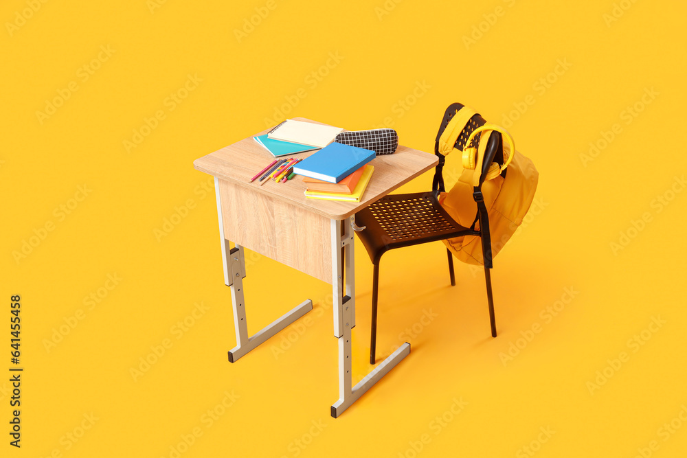 Modern school desk with backpack, headphones and stationery on yellow background