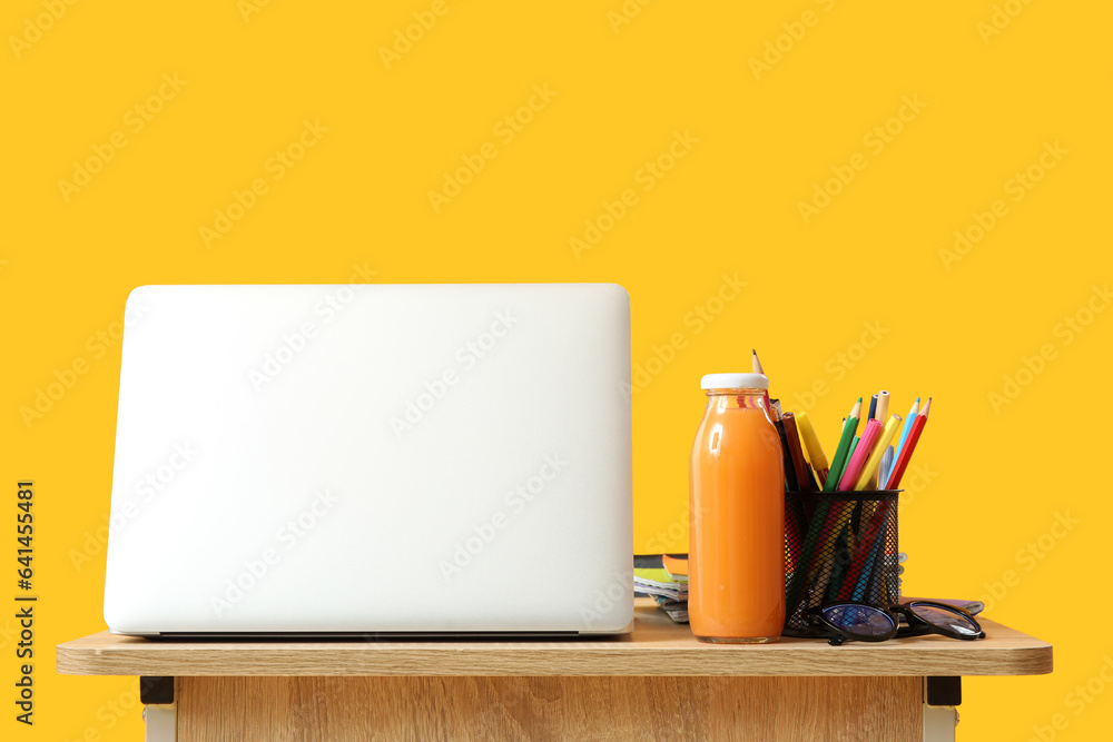 Modern school desk with laptop and stationery on yellow background