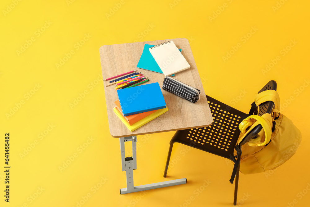 Modern school desk with backpack, headphones and stationery on yellow background