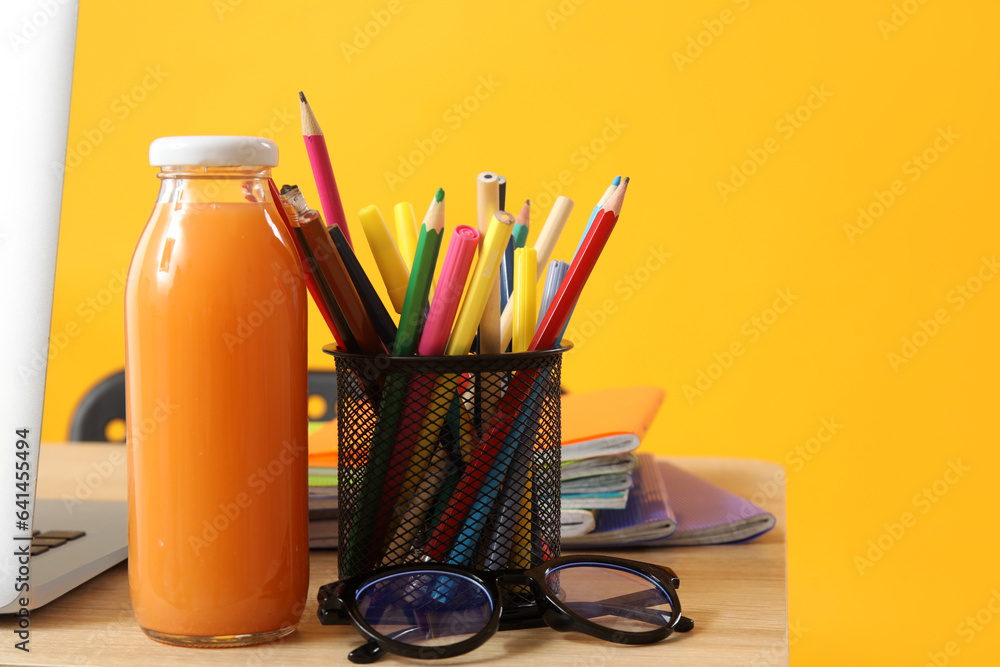 Modern school desk with laptop and stationery on yellow background