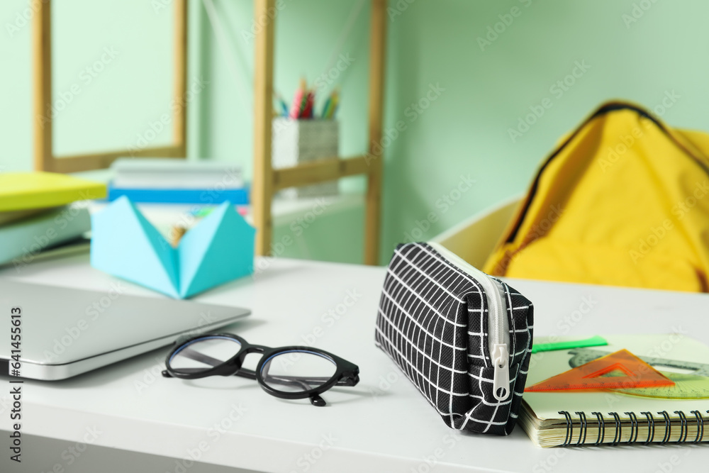 Modern school desk with backpack, laptop and stationery in room near green wall