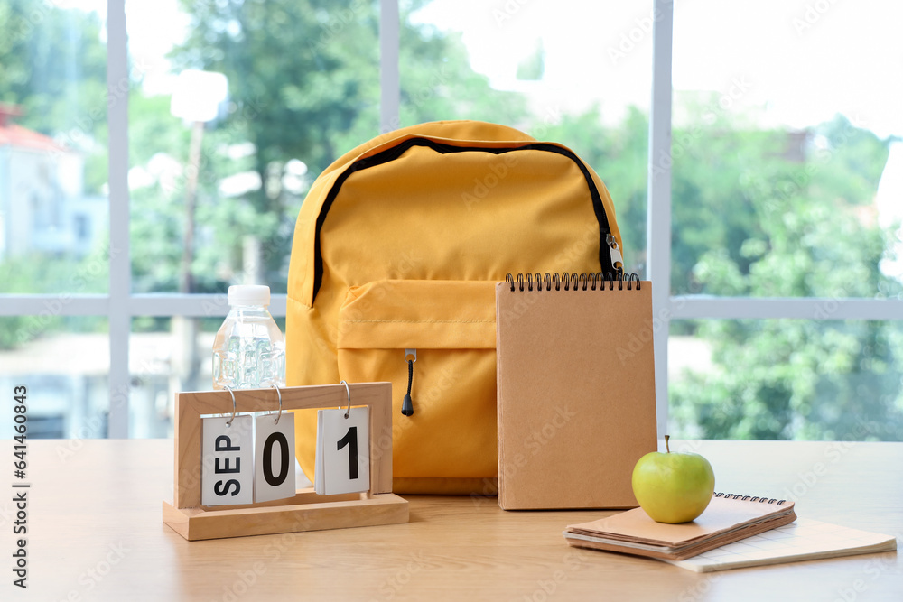 Yellow school backpack with stationery and calendar on brown wooden table near window in classroom