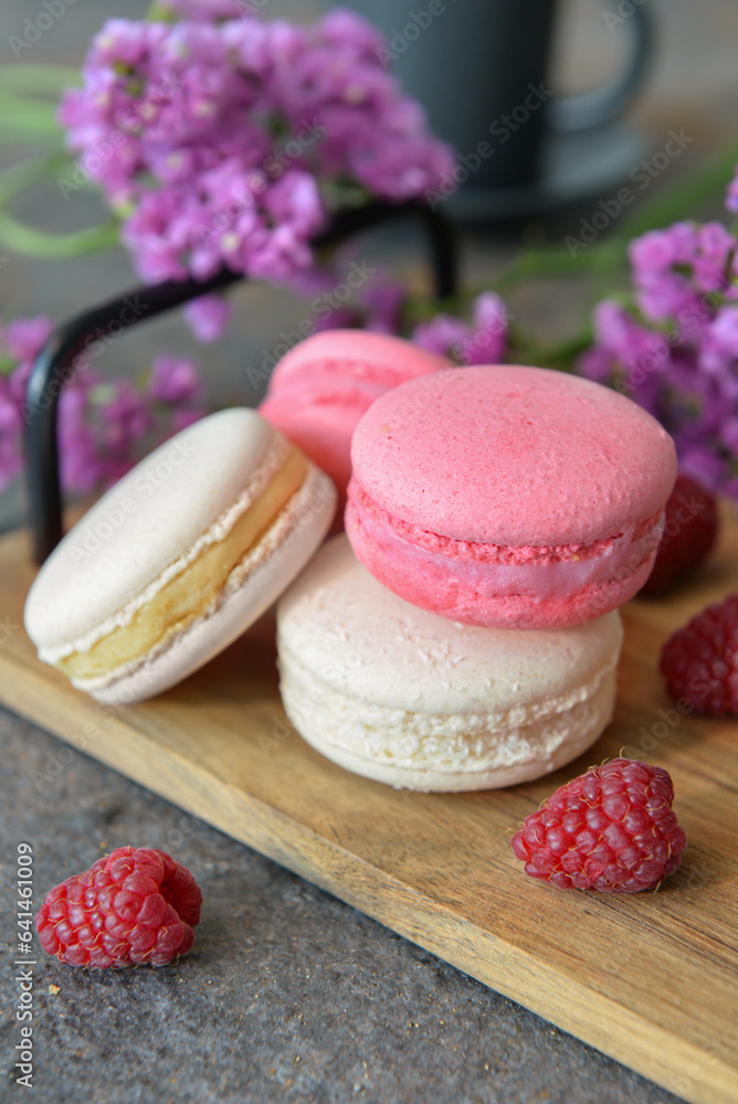 Wooden tray with sweet macaroons and raspberries on dark background