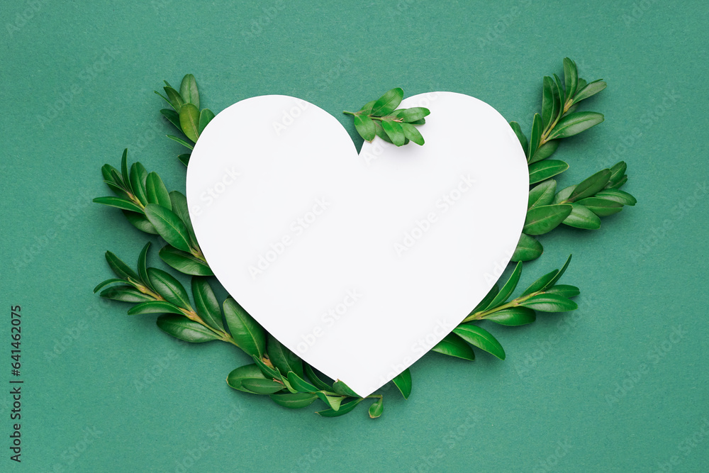 Blank heart shaped card and green leaves on color background