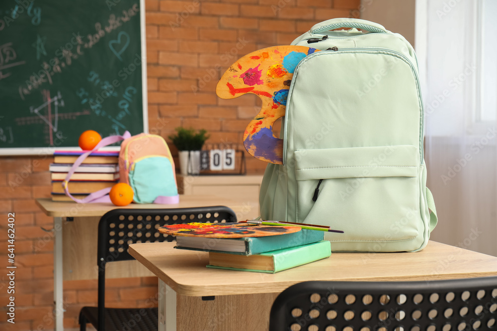 Stylish school backpacks with stationery on desks in classroom