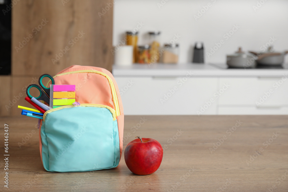 Stylish school backpack with stationery and fresh apple on table in kitchen