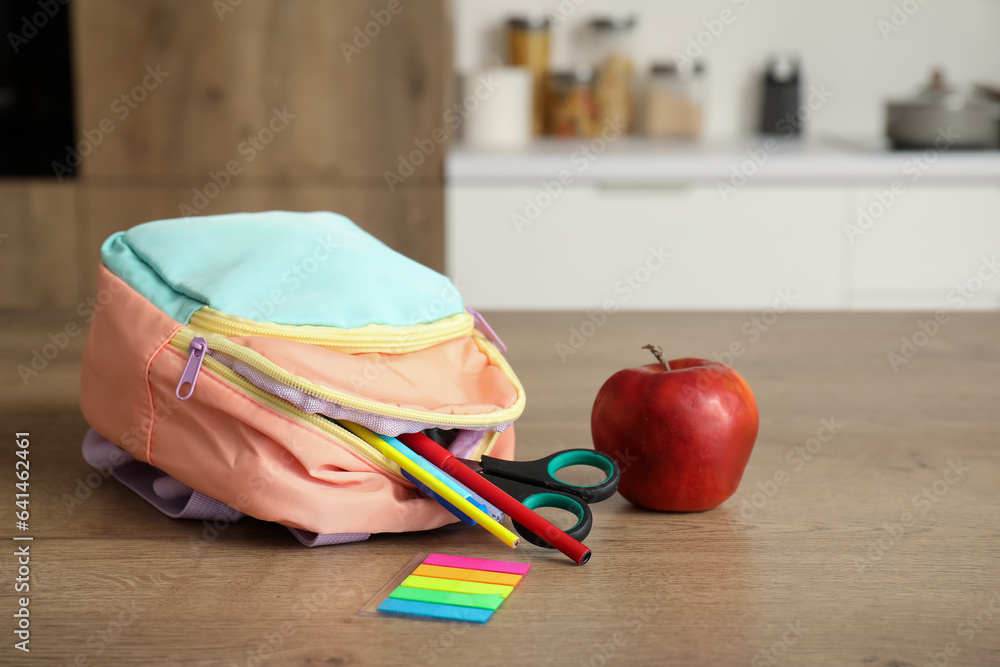 Stylish school backpack with stationery and fresh apple on table in kitchen