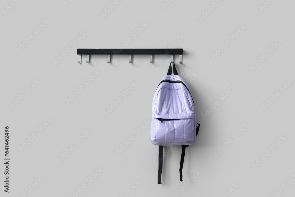 Stylish school backpack hanging on white wall in room