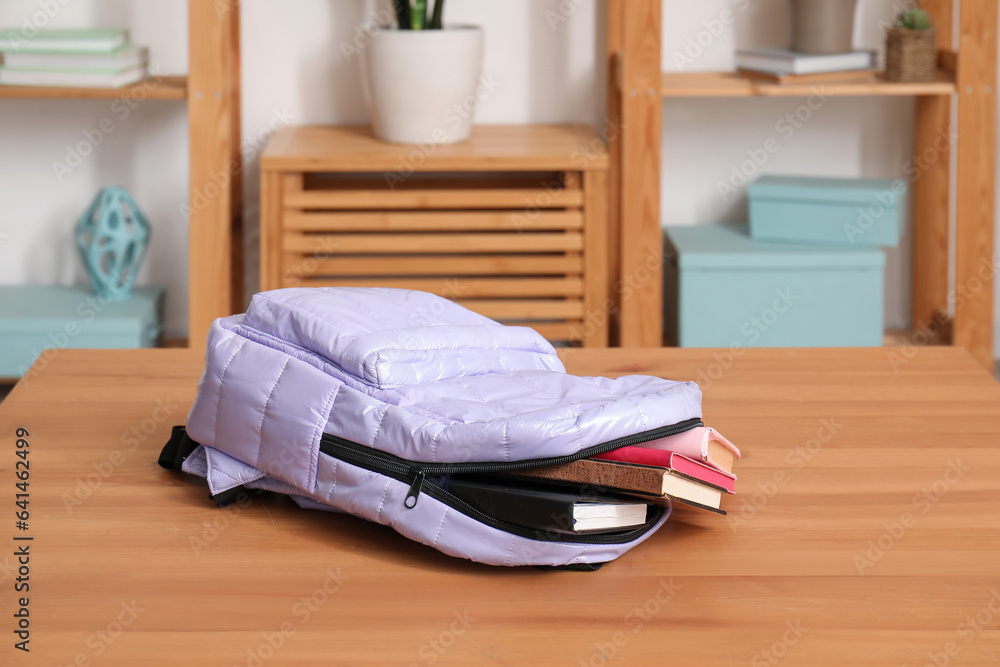 Stylish school backpack with books on wooden table in living room