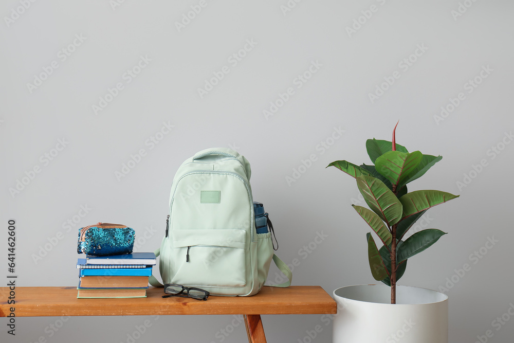 School backpack, stationery, eyeglasses and houseplant on wooden table near light wall